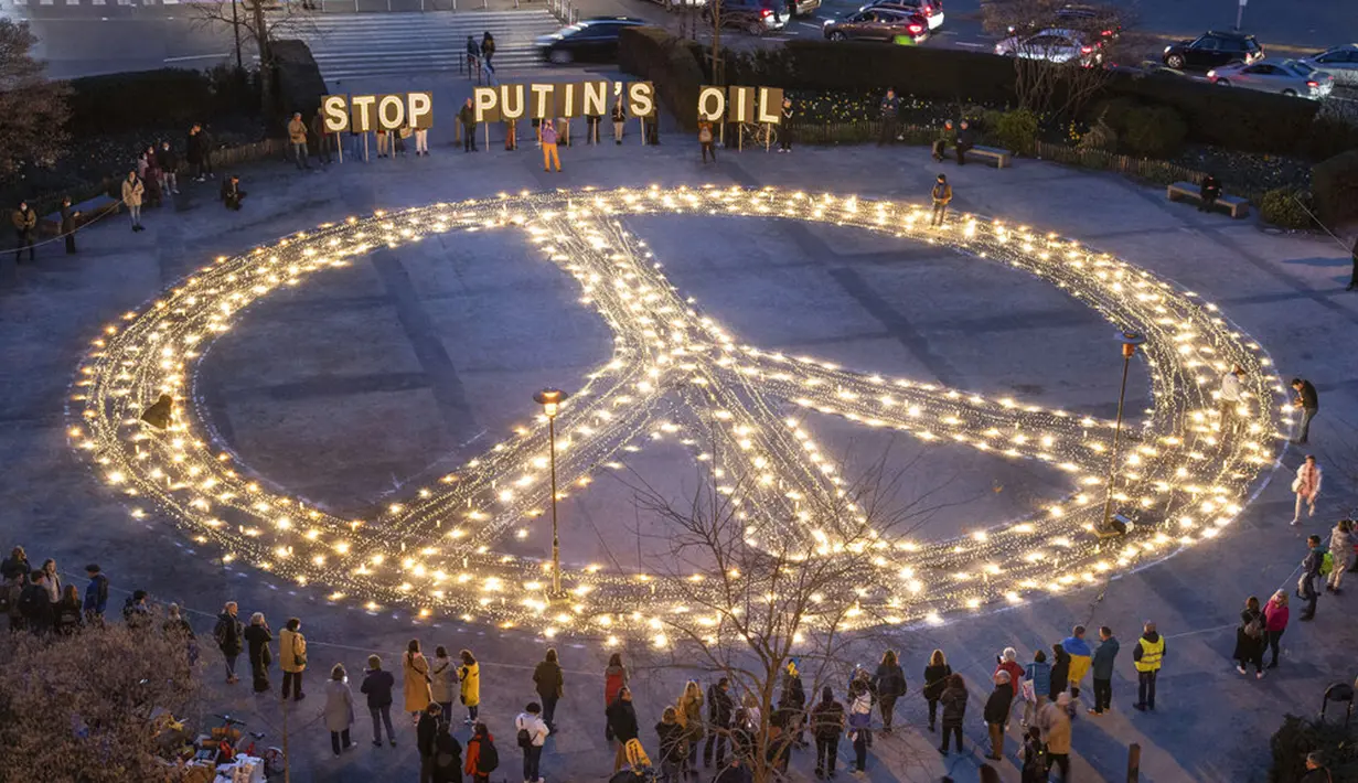 Orang-orang berdiri sekitar tanda perdamaian raksasa dengan pesan 'Hentikan Minyak Putin' jelang KTT Uni Eropa dan NATO di Brussels, Belgia, 22 Maret 2022. Pengunjuk rasa meminta para pemimpin Uni Eropa memberlakukan larangan penuh terhadap bahan bakar Rusia. (AP Photo/Geert Vanden Wijngaert)