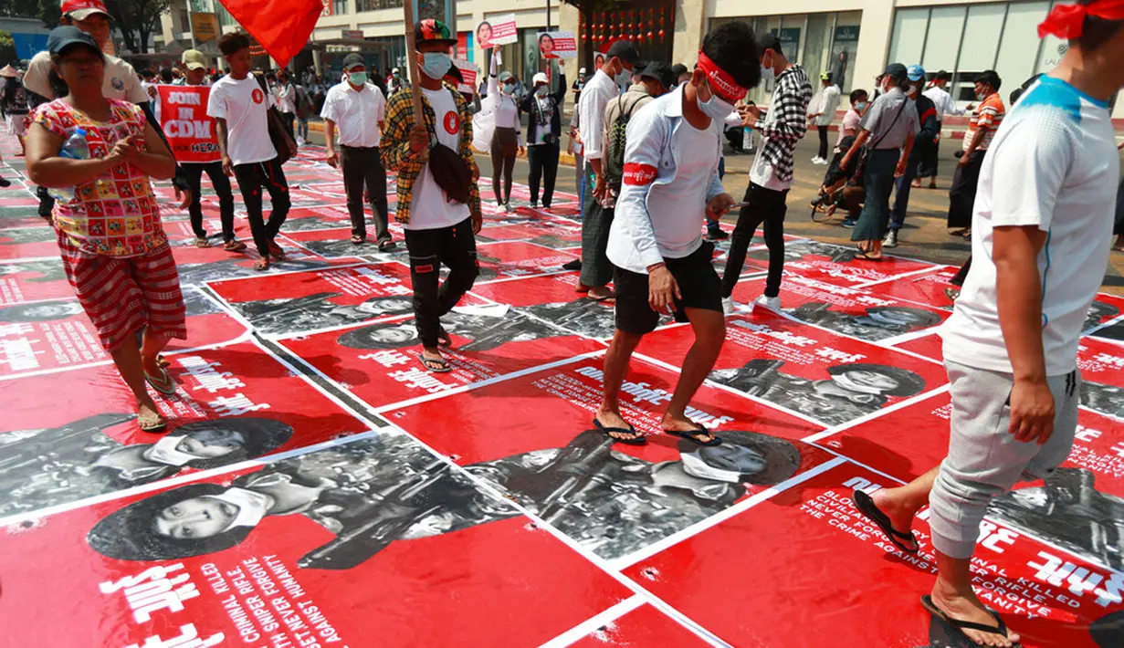 Pengunjuk rasa antikudeta menginjak poster dengan gambar seorang tentara dan tanda Burma bertuliskan "teroris bersenjata" di sebuah jalan di Yangon, Myanmar, Senin (22/2/2021). Peringatan turut diberikan dalam bahasa Inggris yang memperingatkan pendemo terhadap "kekerasan dan anarki." (AP Photo)