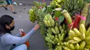 Seorang wanita membeli pisang di sepanjang jalan di Phnom Penh (13/10/2021). Tiga spesies pisang  kuning, gula dan hijau semuanya banyak ditanam di Kamboja. (AFP/Tang Chhin Sothy)