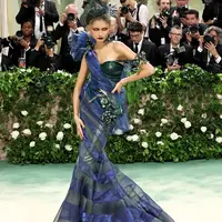 Di Met Gala 2024, Zendaya menghadirkan dua tampilan. Pertama, ia muncul mengenakan gaun couture khusus dari Maison Margiela Artisanal oleh John Galliano. Gaun hijau zamrud dan biru elektrik didesain khusus menggunakan organza dan lame warna sage yang dibuat dari korset satin duchess dengan detail metalik yang dilukis tangan, tirai dan pita berlapis dari aluminium dan organza warna-warni, semuanya diselesaikan dengan tangan. Sedangkan topinya yang terdiri dari kerudung dilukis tangan dan dihiasi dengan stoking adalah rancangan Stephen Jones untuk Maison Margiela dan sepatu Tabi custom dari Christian Louboutin untuk Maison Margiela. [Foto: TeenVogue]