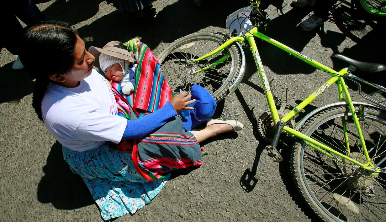 Seorang peserta beristirahat dengan bayinya setelah menyelesaikan balapan sepeda Cholita di El Alto, La Paz, Bolivia (29/10). Balapan ini bertujuan memperkuat budaya setempat dan memberikan kesempatan olahraga bagi kaum wanita. (Reuters/David Mercado)