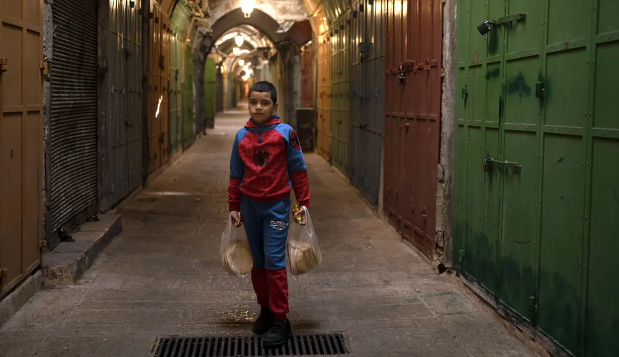 Seorang anak Palestina berpose dengan roti di deretan etalase toko yang ditutup untuk pemogokan umum yang menyerukan gencatan senjata di Gaza di Kota Tua Yerusalem, Senin (11/12/2023). (AP Photo/Maya Alleruzzo)