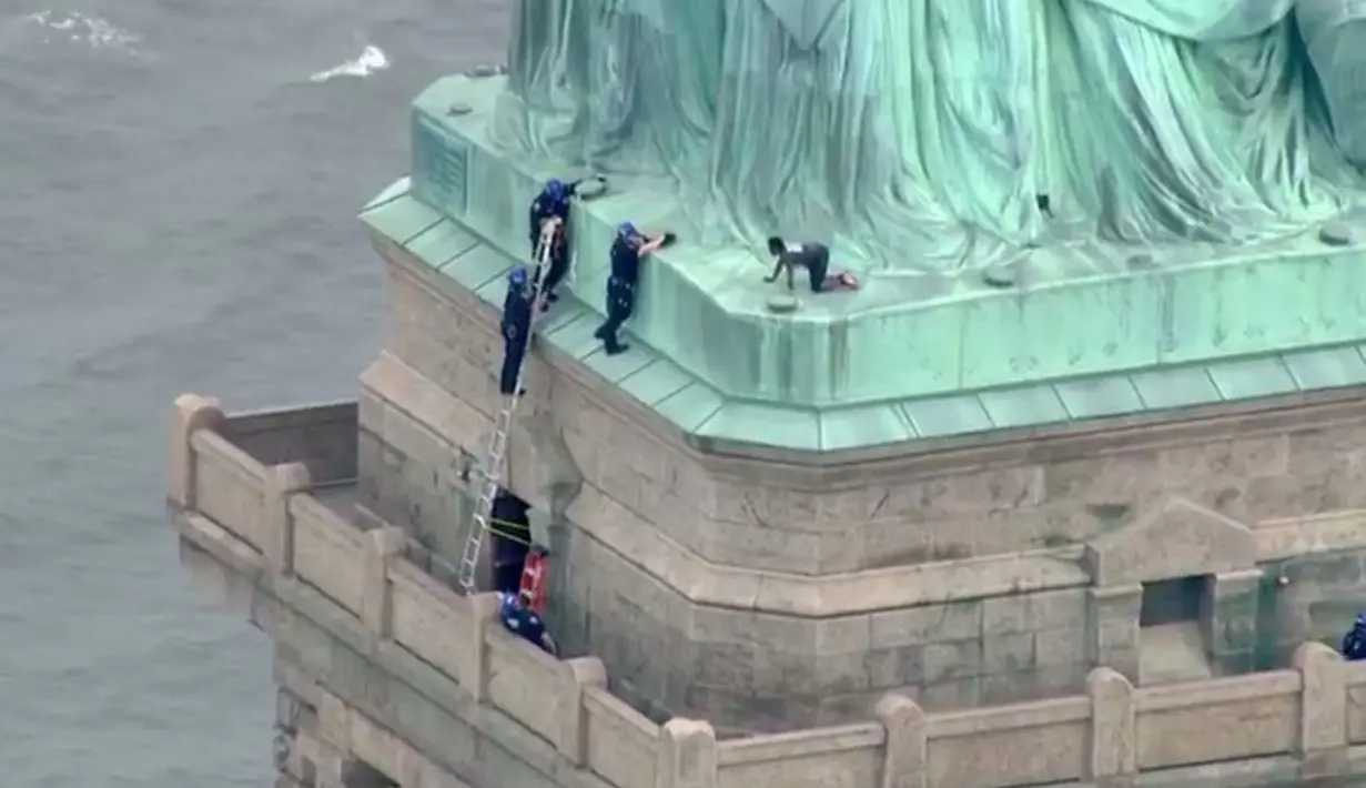 Petugas kepolisian membujuk seorang wanita yang nekat memanjat Patung Liberty di New York, Rabu (4/7). Aksi protes wanita bernama Therese Okoumou ini telah memicu ketegangan dengan para petugas berwenang selama hampir empat jam. (AFP/PIX11 News/HO)
