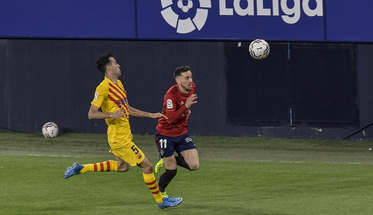 Penyerang Osasuna, Kike Barja membawa bola dari kejaran gelandang Barcelona, Sergio Busquets pada pertandingan lanjutan La Liga Spanyol di stadion El Sadar di Pamplona, Minggu (7/3/2021). Barcelona sukses menjaga jarak dua poin dengan pemuncak klsemen Atletico Madrid. (AP Photo/Alvaro Barrientos)