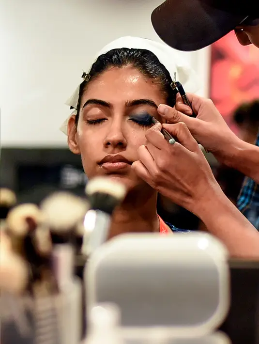 Seorang model India saat dirias oleh kru makeup di belakang panggung sebelum tampil di catwalk selama Lakmé Fashion Week (LFW) Summer Resort 2019 di Mumbai, India (31/1). (AFP Photo/Sujit Jaiswal)
