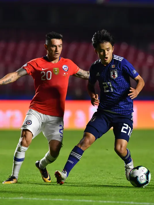 Gelandang Jepang, Takefusa Kubo menggiring bola dari kawalan pemain Chile, Charles Aranguiz selama pertandingan grup C Copa America 2019 di Stadion Morumbi, Sao Paulo, Brasil (17/6/2019). Kubo resmi dikontrak selama enam tahun oleh Real Madrid. (AFP Photo/Nelson Almeida)