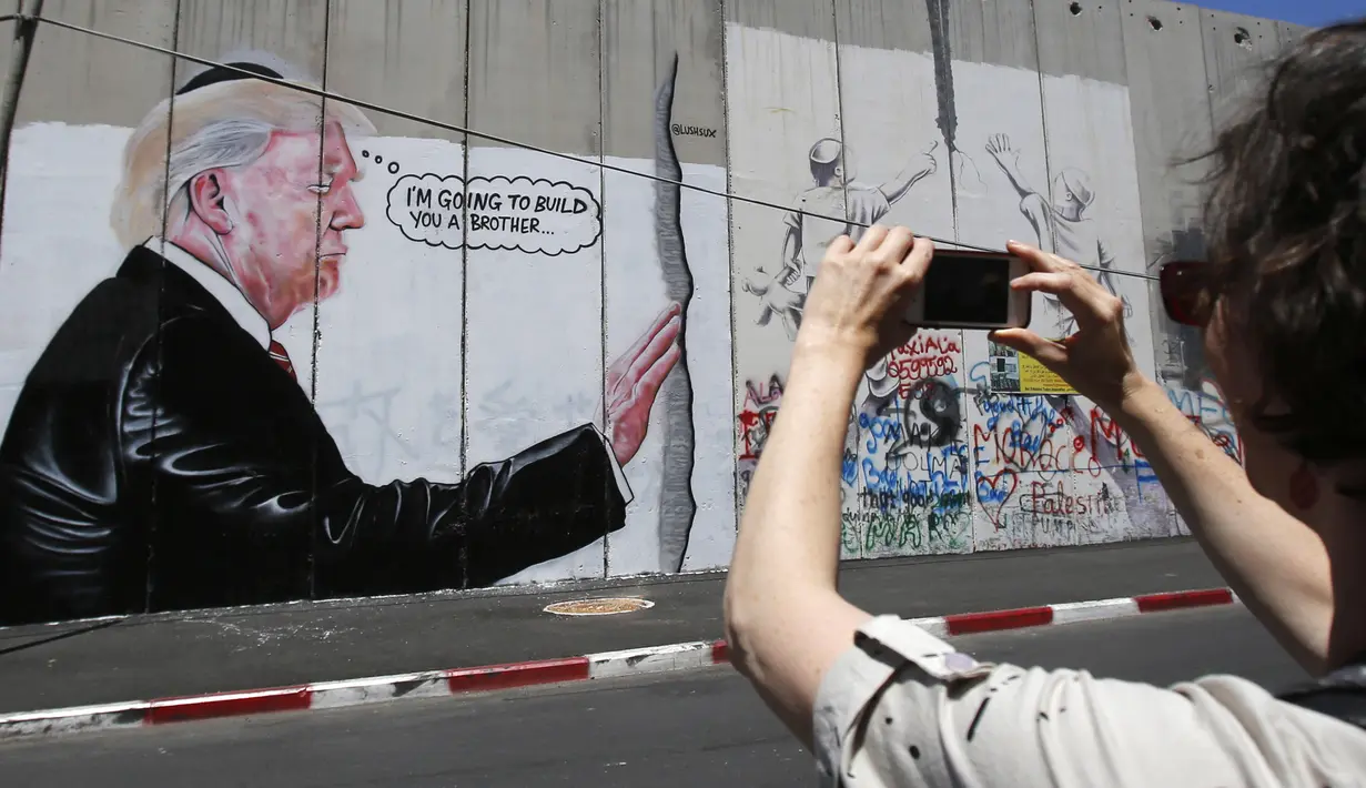 Seorang pengendara motor melintas didepan grafiti yang menggambarkan Presiden AS Donald Trump di tembok pemisah Israel - Palestina di kota Bethlehem (4/8). (AFP Photo/Musa Al Shaer)