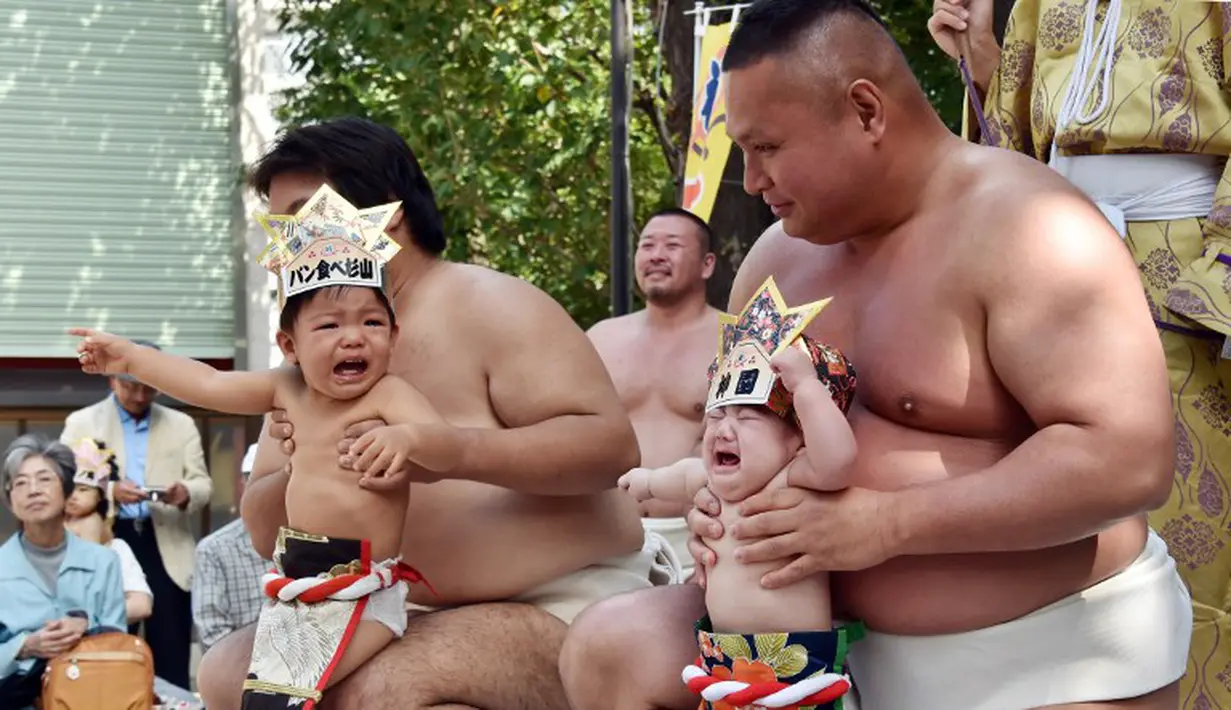 Dua orang bayi menangis saat digendong pegulat sumo dalam Lomba Bayi Menangis di kuil Irugi, Jepang, (21/9/14). (AFP PHOTO/ Yoshikazu TSUNO)