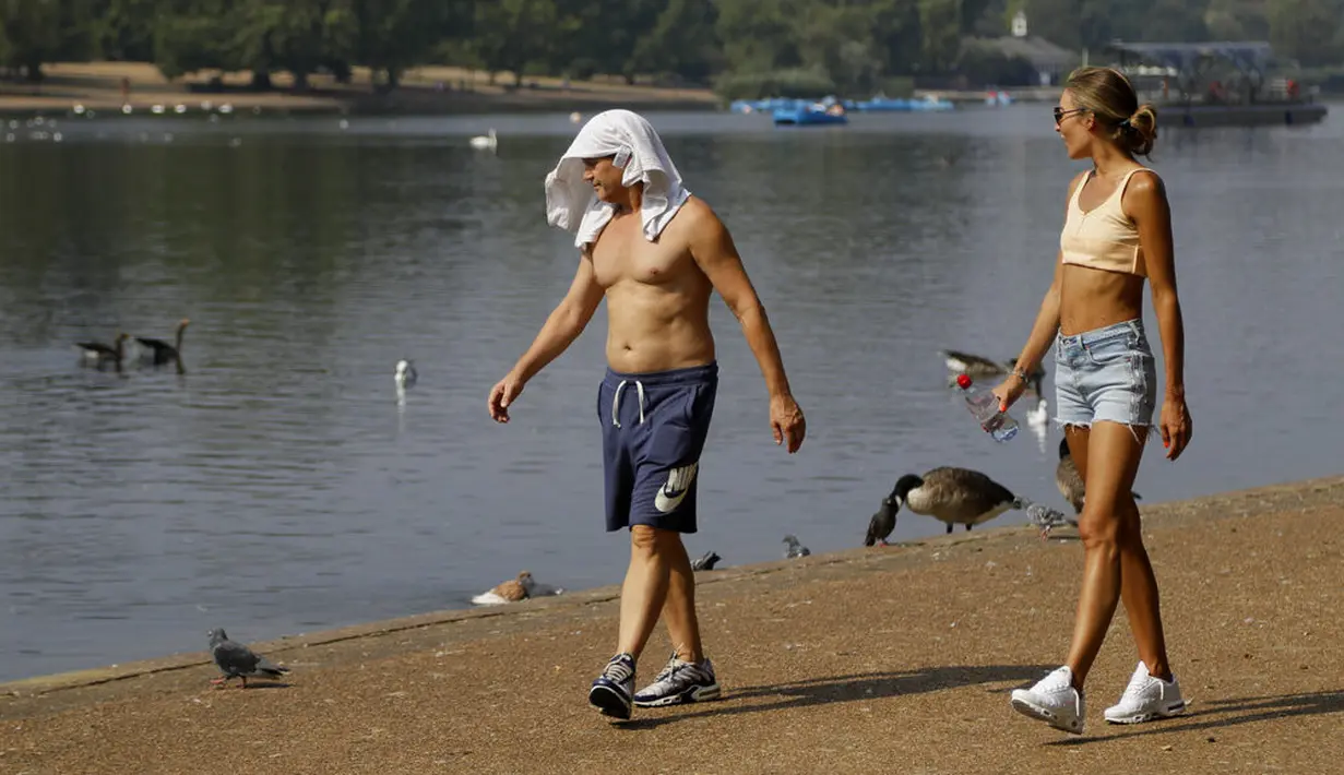 Seorang pria dan wanita berjalan menikmati suasana sungai Serpentine di Hyde Park di London, Rabu, (12/8/2020). Peringatan badai masih berlaku untuk sebagian besar Inggris pada hari Rabu, sementara suhu tinggi diperkirakan lagi di banyak bagian Inggris. ( AP Photo / Kirsty Wigglesworth)