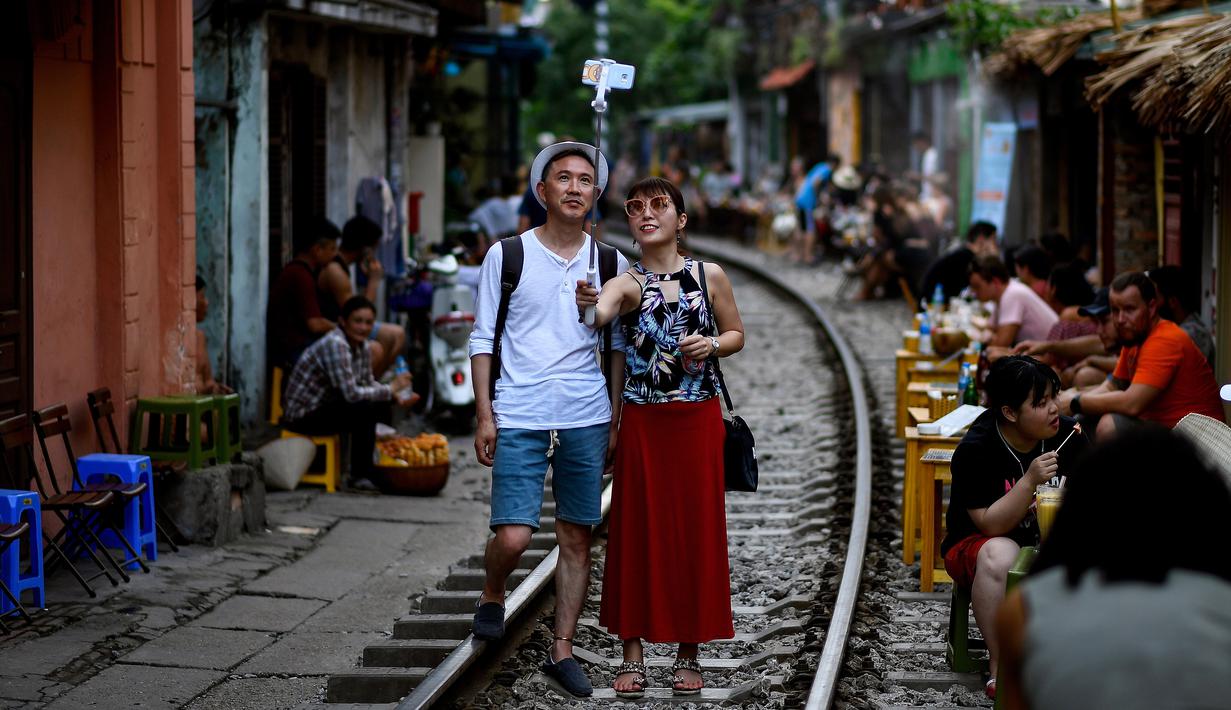 Foto pada 8 Juni 2019 memperlihatkan wisatawan berswafoto di tengah jalur kereta api populer di Hanoi. Di ibu kota Vietnam tersebut rel-rel kereta yang berada di permukiman padat penduduk dijadikan destinasi wisata selfie. (Photo by Manan VATSYAYANA / AFP)