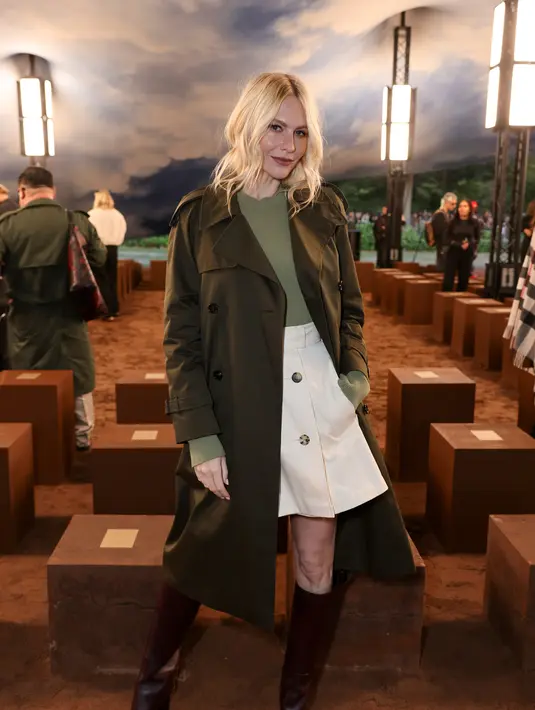 Poppy Delevinge tampak awet muda dengan long sleeve hitam dan rok mini berkancing ganda. Ia lengkapi busananya dengan trench coat berwarna gelap dan boots tinggi [Burberry]