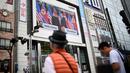 Pejalan kaki melihat layar yang menampilkan pertemuan antara pemimpin Korea Utara Kim Jong-un dan Presiden AS Donald Trump di Tokyo, Selasa (12/6). Untuk pertama kalinya dalam sejarah, Donald Trump dan Kim Jong-un bertemu. (AFP PHOTO/Martin BUREAU)