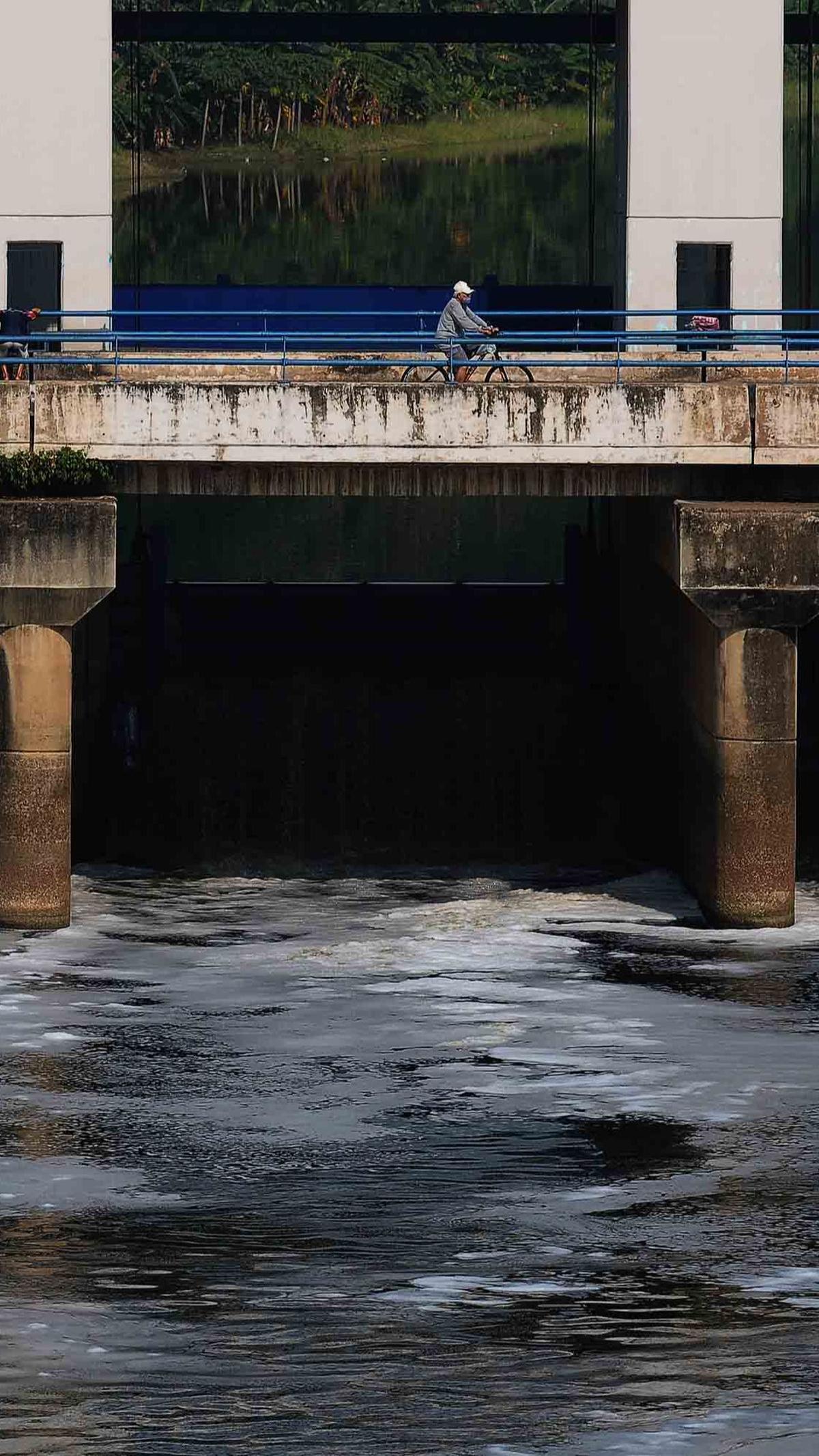 Pengguna sepeda melintas di atas jembatan pintu air Malaka Sari saat busa putih yang berasal dari limbah deterjen mengalir di Kanal Banjir Timur (KBT).