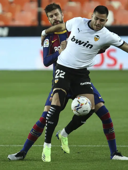 Bek Barcelona, Gerard Pique berusaha merebut bola dari pemain Valencia, Maxi Gomez pada pertandingan La Liga Spanyol di stadion Mestalla, Senin (3/5/2021). Barcelona menang tipis atas Valencia 3-2. (AP Photo/Alberto Saiz)