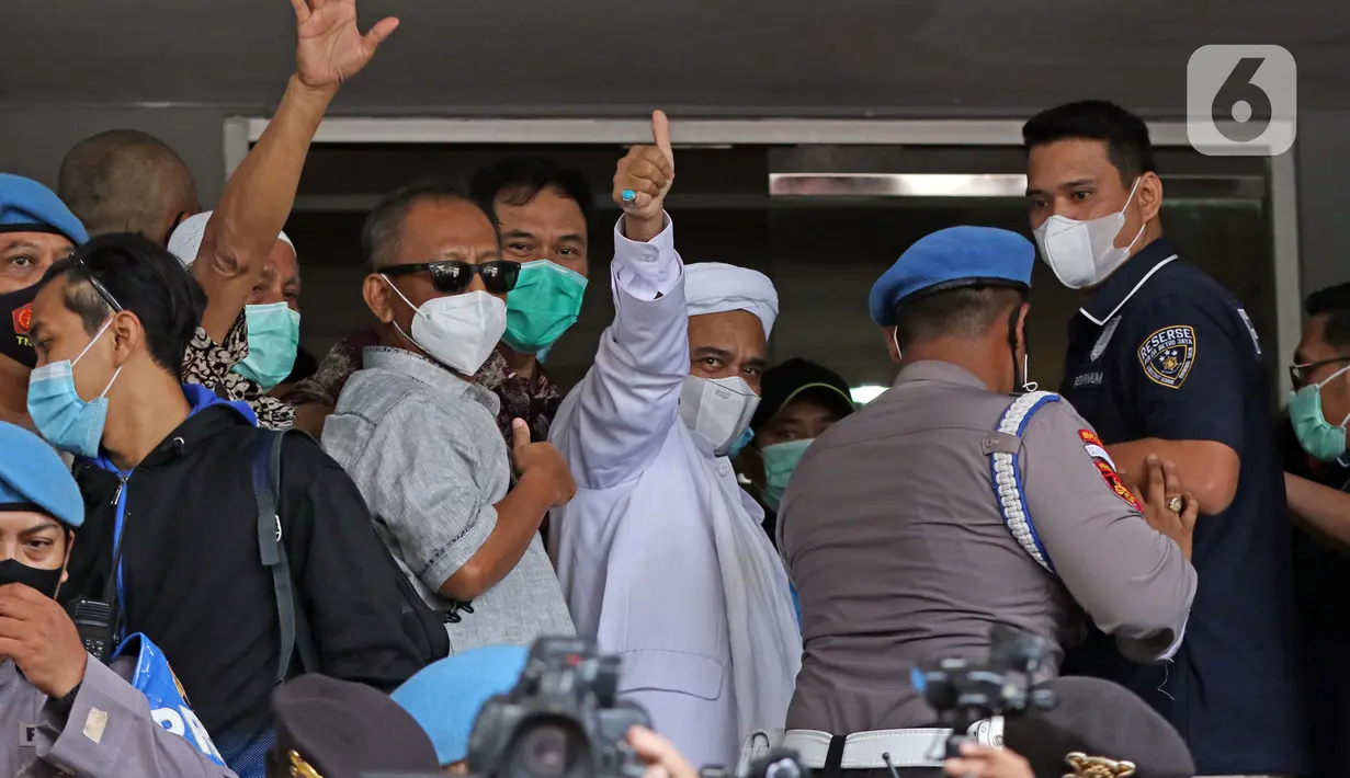 Rizieq Shihab (tengah) melambaikan tangan sesaat sebelum masuk gedung utama Mapolda Metro Jaya, Jakarta, Sabtu (12/12/2020). Rizieq Shihab akan menjalani pemeriksan sebagai tersangka penghasutan dan kerumunan di tengah pandemi Covid-19. (Liputan6.com/Helmi Fithriansyah)