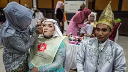 Pasangan pengantin dirias saat akan mengikuti nikah massal di Surabaya, Jawa Timur, Rabu (18/12/2019). Sebanyak 60 pasangan pengantin mengikuti nikah massal yang digelar Dinas Sosial Kota Surabaya. (JUNI KRISWANTO/AFP)