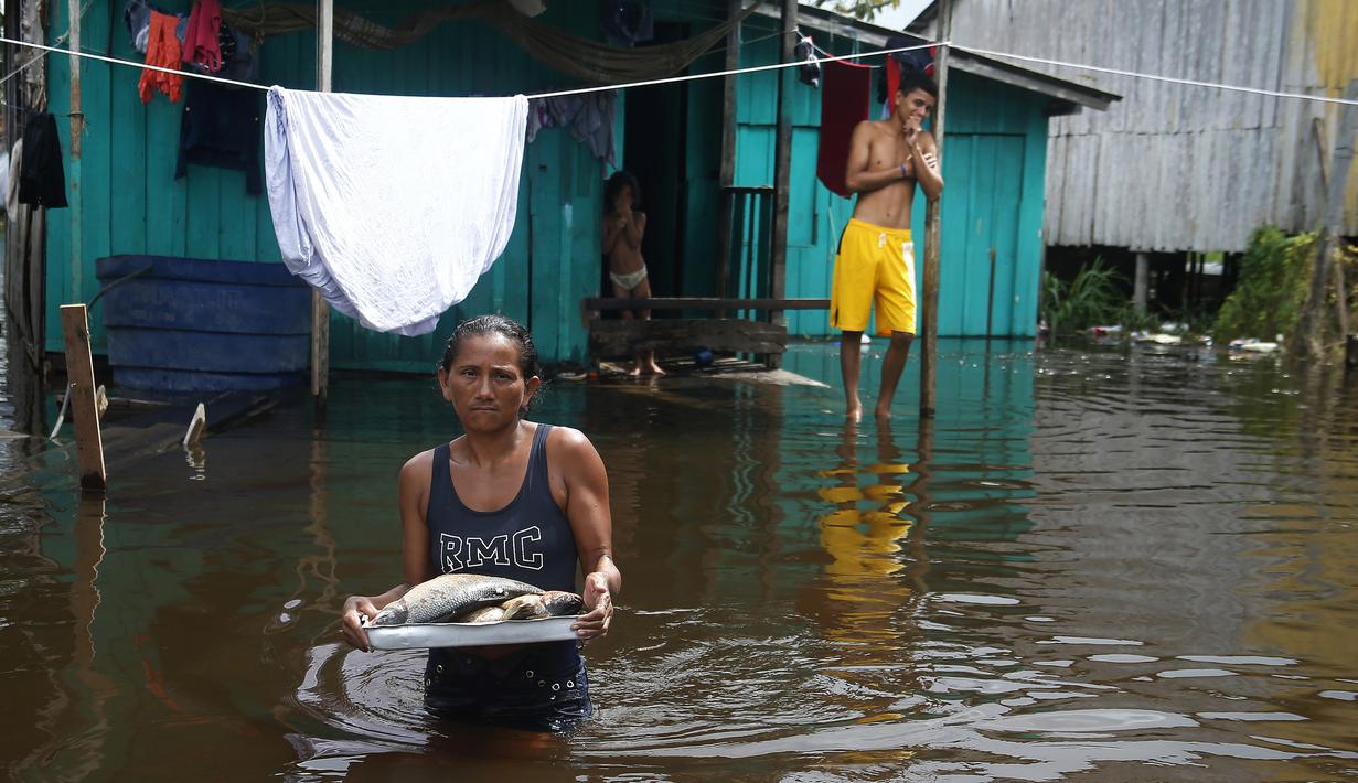 Edileuza Pereira da Silva membawa piring berisi ikan untuk dimasak di luar rumahnya, dibanjiri oleh naiknya sungai Negro di Iranduba, negara bagian Amazonas, Brasil, Senin (23/5/2022). Wilayah Amazon sedang dilanda banjir dengan 35 kotamadya yang menghadapi salah satu banjir terburuk mereka dalam beberapa tahun dan permukaan air diperkirakan akan meningkat selama beberapa bulan mendatang. (AP Photo/Edmar Barros)