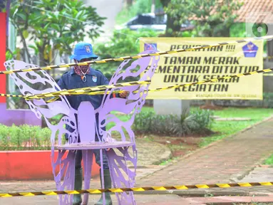 Petugas Dinas Lingkungan Hidup dan Kebersihan (DLHK) Kota Depok memasang garis larangan melintas umum di Taman Merak, Limo, Depok, Senin (25/1/2021). Pembatasan dan penutupan taman tersebut dilakukan dalam rangka Pemberlakuan Pembatasan Kegiatan Masyarakat (PPKM). (merdeka.com/Arie Basuki)