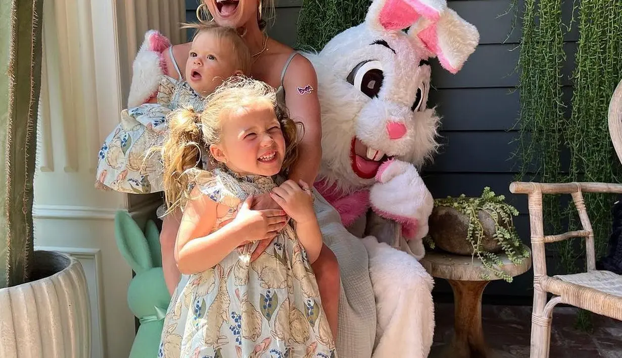 Hilary Duff berpose bersama kedua anaknya. Dengan outfit seragam, yaitu dress bermotif floral yang cantik, yang menarik adalah boneka kelinci besar berwarna putih di belakang Hilary. Foto: Instagram.