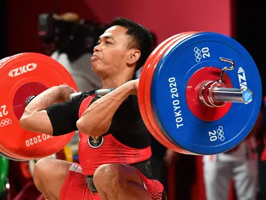 Lifter andalan Indonesia, Eko Yuli Irawan berusaha mengangkat beban saat bertanding dalam kelas 61kg putra Grup A cabor angkat besi Olimpiade Tokyo 2020 di Tokyo International Forum, Minggu (25/7/2021). Eko Yuli meraih medali perak dengan total angkatan 302 kg. (Vincenzo PINTO / AFP)