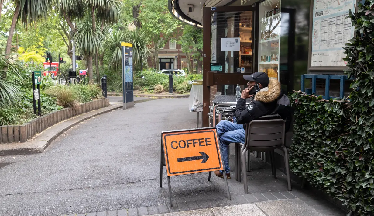 Seorang pria duduk di luar kedai kopi Beatles yang dibuka kembali untuk layanan dibawa pulang (takeaway) di London, Inggris (10/6/2020). Beberapa kedai kopi di Inggris telah dibuka kembali untuk pengiriman atau layanan takeaway dengan mengikuti aturan jaga jarak sosial. (Xinhua/Han Yan)