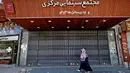 Warga Iran berjalan melewati gedung bioskop yang tutup di pusat kota Teheran, Selasa (20/7/2021). Iran memberlakukan lockdown atau karantina wilayah di ibu kota Teheran dan provinsi terdekat setelah kasus infeksi Covid-19 mencapai rekor tertingginya selama wabah kelima. (ATTA KENARE/AFP)