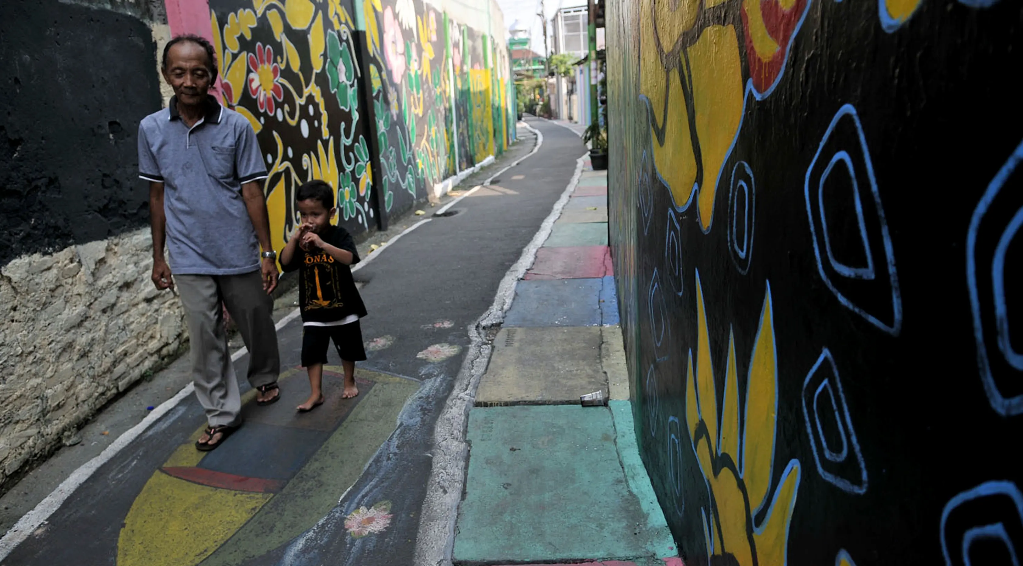 Warga melintas di antara tembok warna-warni di Kampung Pelangi, Johar Baru, Jakarta, Rabu (2/5). (Merdeka.com/Iqbal Nugroho)