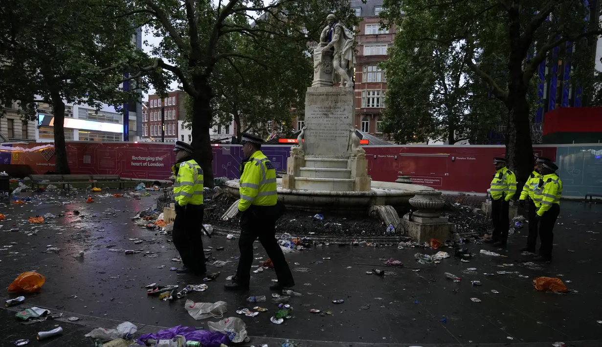 Petugas polisi berdiri di antara sampah yang ditinggalkan penggemar Skotlandia yang berpesta sebelum pertandingan grup D antara Inggris melawan Skotlandia di dekat patung William Shakespeare di Leicester Square di London, Jumat (18/6/2021). (AP Photo/Kirsty Wigglesworth)