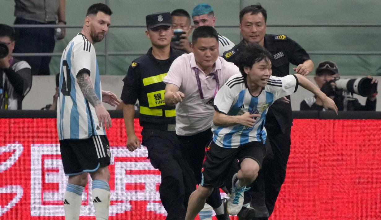 Seorang penyusup lapangan berlari menghindari kejaran petugas setelah memeluk pemain Argentina, Lionel Messi pada laga persahabatan antara Argentina melawan Australia di Workers' Stadium, Beijing, Kamis (15/06/2023). (AP Photo/Mark Schiefelbein)