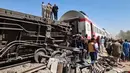 Orang-orang berkumpul di sekitar reruntuhan dua kereta yang bertabrakan di distrik Tahta di provinsi Sohag, sekitar 460 km (285 mil) selatan ibu kota Mesir, Kairo (26/3/2021). Dilaporkan tabrakan ini menewaskan sedikitnya 32 orang dan melukai banyak lainnya. (AFP)