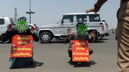 Dua pria mengenakan topeng bergambar virus corona dan memegang plakat bertuliskan "Jangan keluar, jangan mendekati corona" sebagai hukuman karena keluar rumah selama pemberlakukan penguncian wilayah (lockdown) di Chennai, India, Rabu (1/4/2020). (Arun SANKAR / AFP)
