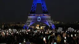 Warga menyaksikan Menara Eiffel yang diterangi dengan warna-warna Israel setelah demonstrasi untuk menunjukkan dukungan kepada Israel di Paris, Prancis, Senin (9/10/2023). Hal ini dilakukan dua hari setelah pejuang Hamas melancarkan serangan multifront yang belum pernah terjadi sebelumnya terhadap Israel yang menewaskan lebih dari 700 orang. (AP Photo/Michel Euler)