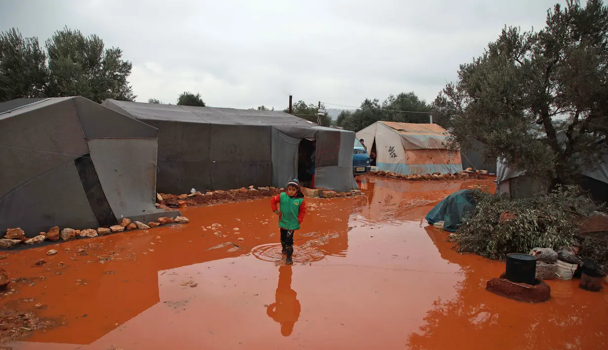 Seorang gadis berjalan melewati genangan air hujan di depan tenda di kamp untuk warga Suriah yang kebanjiran di dekat desa Killi di utara provinsi barat laut Idlib (5/12/2019). (AFP Photo/Aaref Watad)