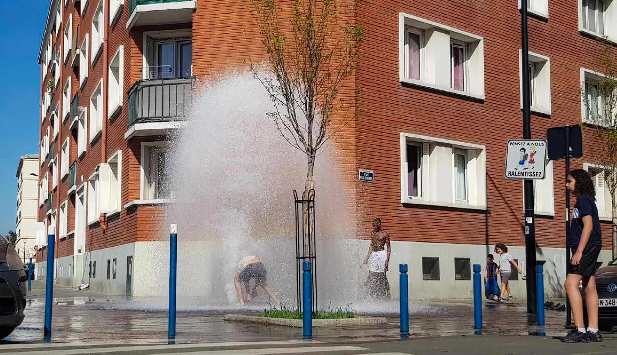 Sejumlah pemuda mendinginkan tubuh di air hidran yang terbuka selama cuaca panas di Aubervilliers, sebelah utara Paris, (19/4). (AFP Photo/Amine Guedaim)