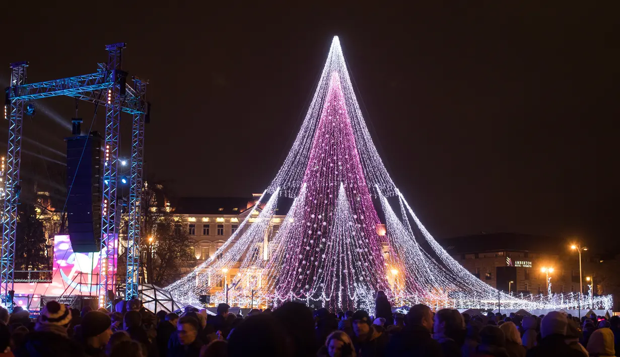 Sejumlah pasangan berdiri di depan pohon Natal raksasa yang menerangi Alun-Alun Katedral di Vilnius, Lithuania, 1 Desember 2017. Pohon Natal megah itu memiliki tinggi sekitar 30 meter yang berhias 70 ribu lampu dan 900 mainan. (AP Photo/Mindaugas Kulbis)