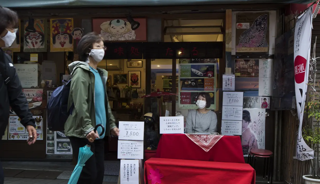 Seorang peramal yang menyebut dirinya Buchiko menunggu pelanggan saat orang-orang berjalan melalui jalan perbelanjaan di Tokyo (15/10/2020). Ibukota Jepang mengonfirmasi lebih dari 280 kasus virus korona baru pada hari Kamis. (AP Photo/Hiro Komae)