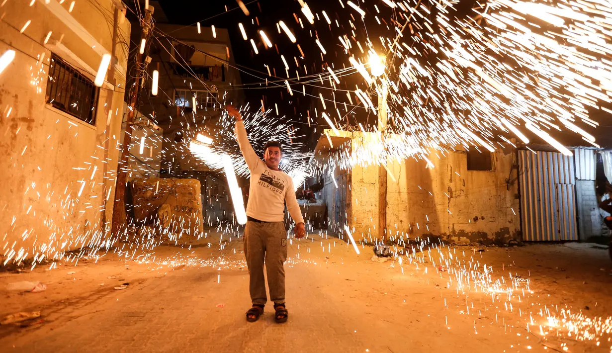 Seorang pemuda Palestina mengayunkan kembang api buatan sendiri, saat orang-orang merayakannya pada malam menjelang bulan suci Ramadan, di Kota Gaza (11/4/2021). (AFP Photo/Mohammed Abed)