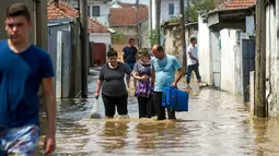 Sejumlah warga melewati jalanan yang banjir akibat hujan deras di Ibu Kota Skopje, Makedonia, Minggu (7/8). Pemerintah menyatakan keadaan darurat sehari setelah setidaknya 21 orang tewas dalam banjir bandang yang disebabkan badai. (Robert ATANASOVSKI/AFP)