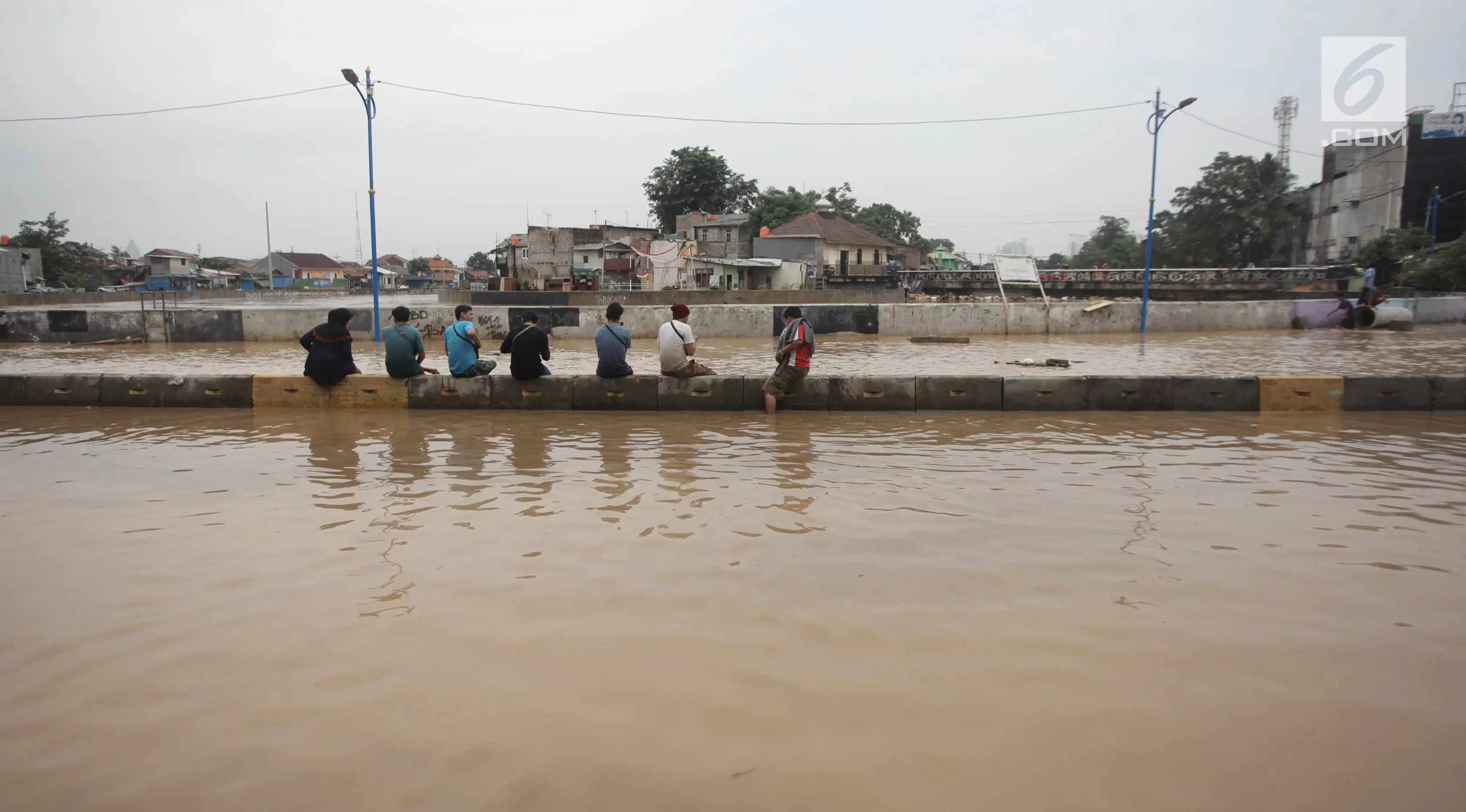 Sejumlah warga duduk di pembatas jalan saat banjir menggenangi Jalan Jatinegara Barat, Jakarta Timur, Selasa (6/2). (Liputan6.com/Arya Manggala)