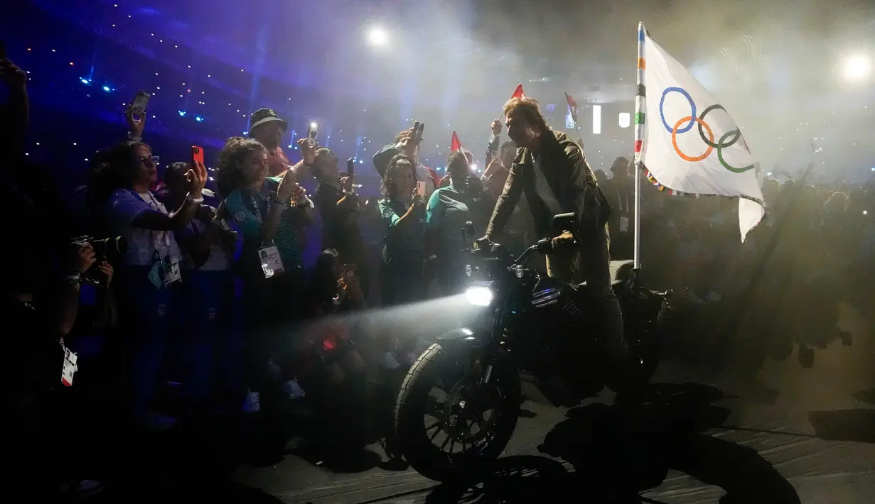 Selanjutnya, Tom Cruise beraksi mengendarai motor sambil membawa bendera Olimpiade. (AP Photo/Ashley Landis)