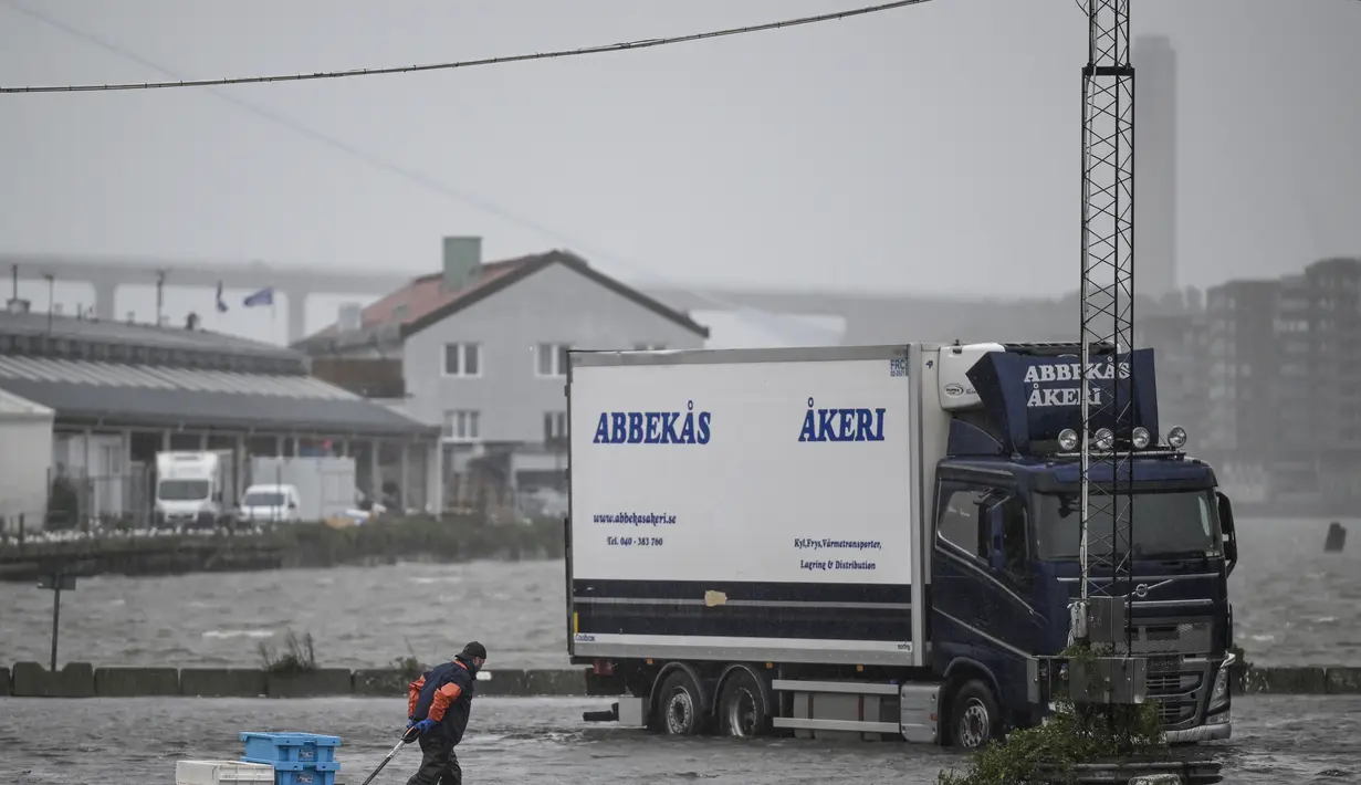 Seorang pria berjalan di sepanjang Fiskhamnen (pelabuhan nelayan) yang banjir setelah sungai Gota Alv meluap akibat hujan deras di Gothenburg, Swedia, Selasa, 8 Agustus 2023.  (Björn Larsson Rosvall/TT News Agency via AP)