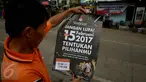 Seorang warga membaca poster yang dibagikan oleh KPU saat sosialisasi Pilkada DKI 2017 di Terminal Senen, Jakarta, Minggu (18/12). Sosialisasi pesta demokrasi ini guna mencegah banyaknya pemilih yang golongan putih atau golput. (Liputan6.com/Johan Tallo)