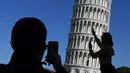 Turis berpose di depan Menara Pisa di kota Pisa, Italia pada 28 November 2018. Setelah upaya yang dilakukan selama lebih dari dua puluh tahun, para insinyur mengatakan kemiringan menara setinggi 57 meter itu telah berkurang 4 cm. (Tiziana FABI / AFP)