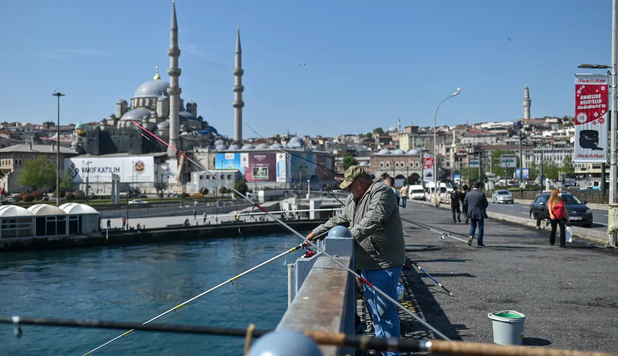 Seorang pria memancing di Jembatan Galata di Istanbul, Turki pada Senin (17/5/2021). Pemerintah Turki mencabut lockdown atau penguncian penuh selama 17 hari untuk mengekang lonjakan infeksi virus corona COVID-19. (OZAN KOSE / AFP)