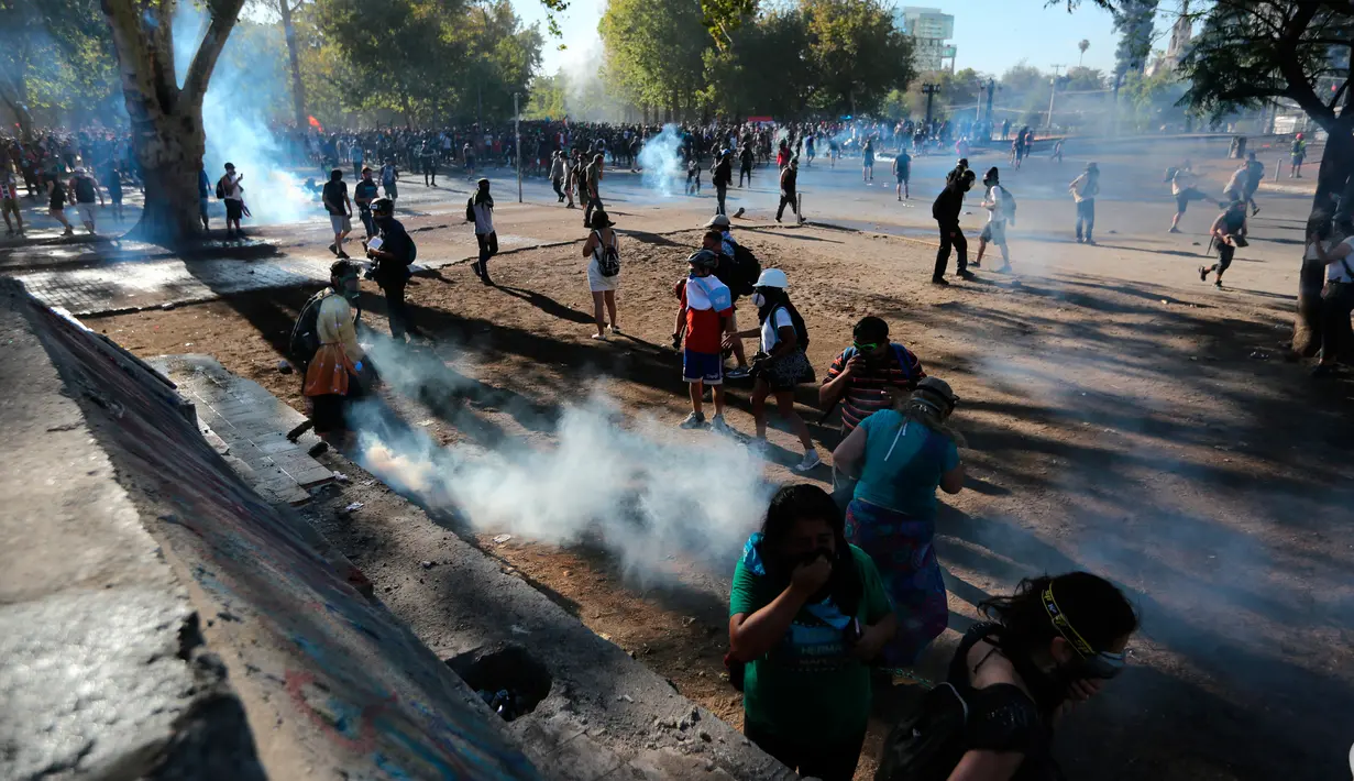 Para demonstran antipemerintah berkumpul di antara gas air mata yang ditembakkan polisi untuk membubarkan protes di Santiago, Chile, Jumat (27/12/2019). Protes Chile berubah menjadi gerakan yang jauh lebih besar dan luas dengan daftar panjang tuntutan. (AP Photo/Fernando Llano)