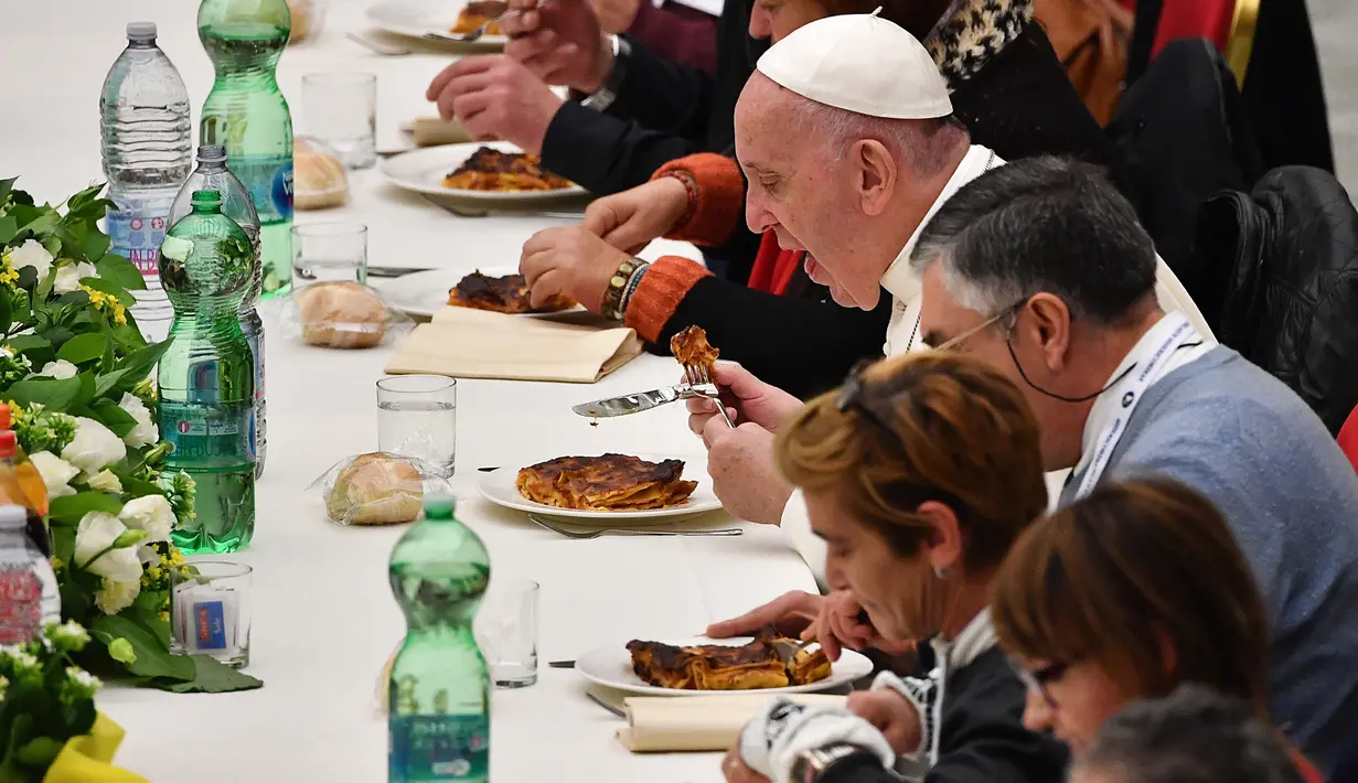Paus Fransiskus (kanan) menyantap makan siang bersama sejumlah orang miskin di Pope Paul VI hall, Vatikan, Minggu (18/11). Makan siang bersama ratusan kaum papa, tunawisma, dan pengangguran itu memperingati Hari Orang Miskin Sedunia. (Vincenzo PINTO/AFP)