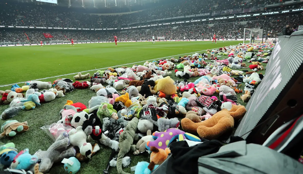 Para pemain mengumpulkan mainan dari lapangan yang dilemparkan oleh suporter Besiktas selama pertandingan Liga Turki (Super Lig) melawan Antalyaspor di stadion Vodafone di Istanbul, Minggu (26/2/2023). Penggemar klub Besiktas melemparkan ribuan boneka mainan ke lapangan sebagai simbol solidaritas dengan anak-anak yang terkena dampak gempa bumi dahsyat di Turki. (Handout / DHA (Demiroren News Agency) / AFP)