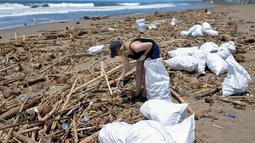 Seorang turis asing mengumpulkan sampah di antara tumpukan puing di pantai di Batu Belig di Kabupaten Badung setelah hanyut menyusul badai lepas pantai di Bali (14/12/2021). (AFP/Sony Tumbelaka)