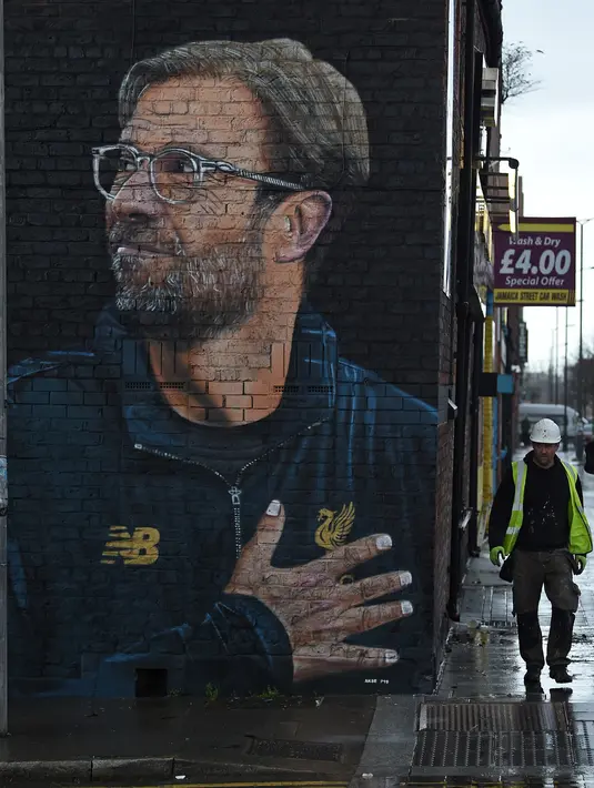 Seorang pekerja melintas dekat mural pelatih klub Liverpool, Jurgen Klopp di Jamaica Street, pusat kota Baltic Triangle di Liverpool, Senin (10/12). Pengerjaan mural itu dimulai sejak 8 November 2018 lalu oleh seniman jalanan "Akse". (Paul ELLIS / AFP)