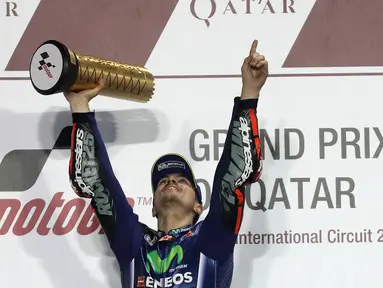 Pembalap Movistar Yamaha MotoGP, Maverick Vinales, mengangkat pialanya di atas podium setelah memenangi MotoGP Qatar di Sirkuit Losail, Doha, Minggu (26/3). Vinales menyelesaikan balapan dengan catatan waktu 38 menit 59,999 detik. (Karim JAAFAR/AFP)